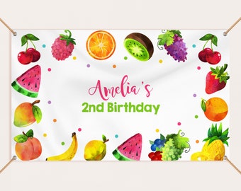 May include: A white banner with watercolor illustrations of various fruits, including cherries, raspberries, oranges, kiwi, grapes, watermelon, mangoes, bananas, and a pineapple. The banner reads "Amelia's 2nd Birthday" in pink and green.