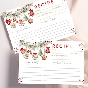 以下が含まれることがあります： 「RECIPE」と赤い文字で書かれた2枚の白いレシピカード。カードは、クリスマスのオーナメントと緑の植物の水彩イラストで装飾されています。「ingredients」という単語は筆記体で書かれています。