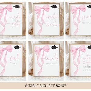 Könnte beinhalten: Ein Set aus sechs gerahmten Tischschildern mit Abschlussfeier-Motiv. Jedes Schild zeigt eine rosa Aquarellschleife und ein Band, eine schwarze Abschlusskappe und Text wie "Karten und Geschenke" und "Süßigkeiten". Die Schilder sind 20 x 25 cm groß.