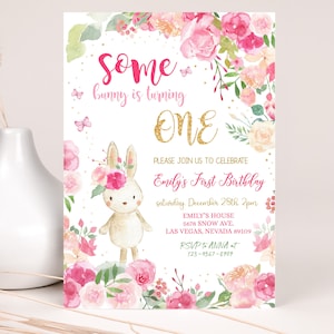 May include: A pink and gold first birthday invitation with a cute bunny rabbit illustration surrounded by pink and white flowers. The text reads "Some bunny is turning ONE. Please join us to celebrate Emily's First Birthday, Saturday, December 28th, 2pm. Emily's House, 5678 Snow Ave., Las Vegas, Nevada 89109. RSVP to Anna at 123-9567-8909."