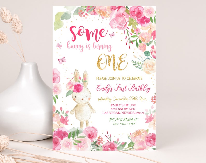 May include: A pink and gold first birthday invitation with a cute bunny rabbit illustration surrounded by pink and white flowers. The text reads "Some bunny is turning ONE. Please join us to celebrate Emily's First Birthday, Saturday, December 28th, 2pm. Emily's House, 5678 Snow Ave., Las Vegas, Nevada 89109. RSVP to Anna at 123-9567-8909."