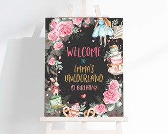 May include: A black chalkboard sign with pink flowers and a whimsical Alice in Wonderland theme. The sign says "Welcome to Emma's Onederland 1st Birthday".