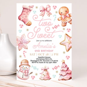 May include: Pink and white birthday invitation with the text "Two Sweet" and "Amelia's 2nd Birthday". The invitation features a gingerbread man, a snowman, a Christmas tree, and other festive decorations.