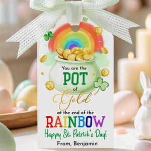 Pode incluir: Uma etiqueta de presente do Dia de São Patrício com uma fita verde. A etiqueta apresenta um pote de ouro no final de um arco-íris, com o texto "You are the POT of Gold at the end of the RAINBOW. Happy St. Patrick's Day! From, Benjamin."