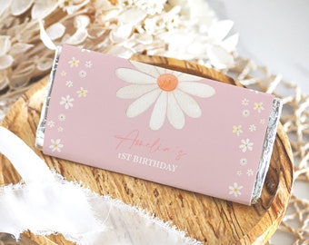 Op de afbeelding: Roze chocolade reep verpakking met een witte madeliefje en kleinere witte madeliefjes langs de zijkant. De verpakking heeft de tekst "Amelia's 1st Birthday".