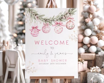 May include: A white welcome sign on an easel, decorated with watercolor-style pink baubles and greenery. The sign reads "Welcome to Emily & James's Baby Shower Saturday 28th December."