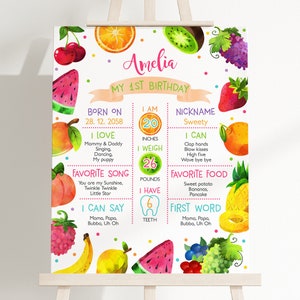 Könnte beinhalten: Ein farbenfroher Obst-First-Birthday-Meilenstein-Poster für ein Mädchen namens Amelia. Das Poster zeigt eine Wassermelone, einen Pfirsich, eine Ananas, eine Banane, eine Kiwi, eine Erdbeere, eine Traube und eine Himbeere. Das Poster enthält Informationen über Amelias Alter, Größe, Gewicht, Lieblingsessen, Lieblingslied und erstes Wort.