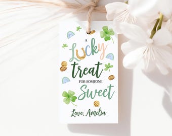 May include: A white gift tag with a watercolor design featuring a horseshoe, shamrocks, rainbows, and gold coins. The text reads "A lucky treat for someone sweet" and "Love, Amelia". The tag is tied with twine.