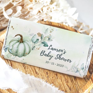 May include: A white chocolate bar wrapper with a watercolor design of a green pumpkin and leaves. The text on the wrapper reads "Lauren's Baby Shower 10.15.2023".