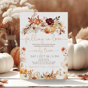 Op de afbeelding: Een baby shower uitnodiging met een aquarel illustratie van pompoenen, bladeren en bloemen in herfstkleuren. De tekst luidt "falling in love" en bevat de datum, tijd en locatie van het evenement.