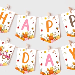 Pode incluir: Uma faixa branca com a palavra "HAPPY" em letras laranja e rosa e a palavra "DAY" em letras rosa. A faixa é decorada com folhas de outono e abóboras.