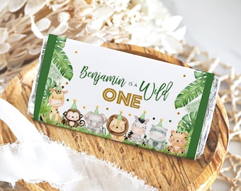 May include: A white chocolate bar wrapper with a green border. The wrapper features a jungle theme with green leaves, gold glitter, and a variety of animals including a giraffe, monkey, elephant, lion, zebra, and tiger. The text on the wrapper reads "Benjamin is a Wild One".