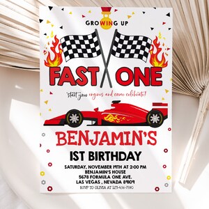 May include: A red, white and black birthday invitation for a 1st birthday party with a racing car theme. The invitation features a red racing car with flames and chequered flags. The text on the invitation reads "Growing Up Fast One" and "Benjamin's 1st Birthday".