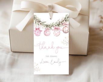 May include: A white gift tag with a watercolor design featuring pink Christmas ornaments and greenery. The tag reads "thank you for coming, Love, Emily" in delicate pink script, tied to a wrapped gift with a white ribbon.