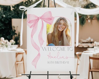 Peut inclure: Panneau de bienvenue blanc pour un 16e anniversaire. Il présente un nœud et des rubans roses à l'aquarelle, une photo d'une jeune femme souriante et le texte "WELCOME TO Amelia's 16TH BIRTHDAY". Le panneau est sur un chevalet noir.