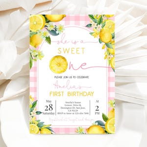 Könnte beinhalten: Eine Einladungskarte mit rosa und weißem Karomuster, Zitronen und Blumen. Der Text lautet "She is a Sweet One" und "Amelia's First Birthday". Das Datum ist Samstag, der 28. Mai, um 14:00 Uhr.