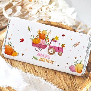May include: A white chocolate bar wrapper with a pink tractor carrying pumpkins and fall leaves. The text on the wrapper reads "Amelia's 2nd Birthday".