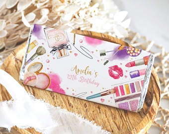 May include: A white chocolate bar wrapper with a pink, purple, and gold design featuring makeup items like lipstick, eyeshadow palettes, and perfume bottles. The text "Amelia's 12th Birthday" is printed on the wrapper.