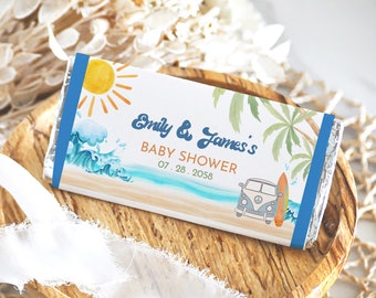 Op de afbeelding: Een witte chocolade reep verpakking met een blauwe rand. De verpakking heeft een strand scène met een zon, golven, palmbomen en een vintage busje met een surfboard. De tekst op de verpakking is "Emily & James's Baby Shower 07.28.2058".