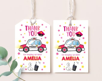 May include: Two pink and white thank you tags with a cartoon police car, a police hat, handcuffs, and a walkie talkie. The text on the tags reads "Thank You" and "for keeping us safe! Amelia".