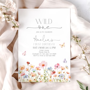 以下が含まれることがあります： 「WILD one」と「Amelia's FIRST BIRTHDAY」の文字が入った白い招待状。水彩画のフローラルボーダーと蝶が特徴です。招待状には、イベントの日時と場所が記載されています。
