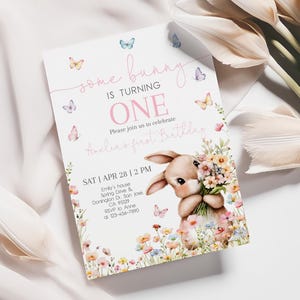 May include: A pink and white invitation card with a bunny holding flowers. The card says "some bunny is turning one" and has butterflies and flowers on it. The text also says "Please join us to celebrate Anelia's first birthday" and includes the date, time, and location of the party.