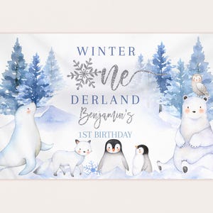 Può includere: Uno striscione bianco con un tema invernale. Presenta un fiocco di neve blu e bianco, le parole "Winter One", "Derland Benjamin's" e "1st Birthday", insieme a illustrazioni di un orso polare, una foca, un pinguino e una volpe.