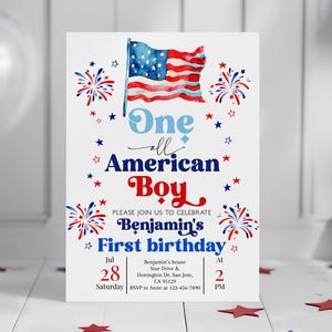 Op de afbeelding: Een witte uitnodigingskaart met een patriottisch thema. Het toont een aquarel illustratie van de Amerikaanse vlag, vuurwerk en sterren in rood, wit en blauw. De tekst luidt "One all American Boy" en kondigt Benjamin's eerste verjaardag op 28 juli aan.