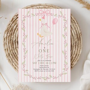 May include: A pink and white striped invitation card with a floral border and a cartoon goose wearing a bow. The text reads "Amelia is ONE Olly Goose" and includes event details.