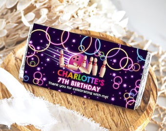 Puede incluir: Un envoltorio de chocolate negro y morado con un diseño de brillo neón. Presenta una bola de bolos y bolos con el texto "Charlotte's 7th Birthday" y "Thank you for celebrating with me!"