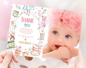 May include: A pink and blue Alice in Wonderland themed thank you card with a photo of a baby girl. The card features a gold frame with illustrations of teacups, a flamingo, a cupcake, and a rabbit. The text on the card reads "Thank You" and "I enjoyed the cake and the presents too, but my favorite part was seeing you! Thank you for coming to my party! Emma Brown."