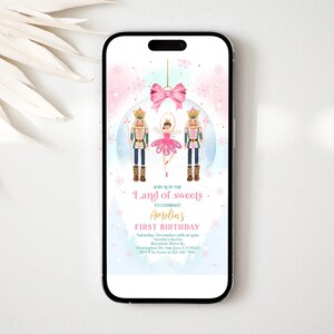 Puede incluir: Una invitación digital para una fiesta de primer cumpleaños con temática de Cascanueces. La invitación presenta una muñeca bailarina bailando con un soldado Cascanueces frente a un adorno rosa y azul. El texto dice "Únete a nosotros en la Tierra de los Dulces para celebrar el primer cumpleaños de Amelia".