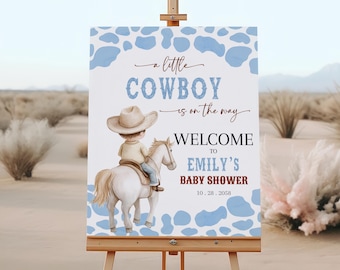 May include: A baby shower welcome sign featuring a watercolor illustration of a child in a cowboy hat riding a white horse. The sign reads "A little cowboy is on the way" and welcomes guests to Emily's baby shower.