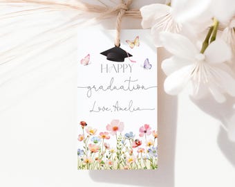 May include: A white graduation gift tag with a black mortarboard, butterflies, and watercolor flowers. The tag reads "Happy graduation Love, Amelia" in elegant script. A decorative floral design adorns the bottom.