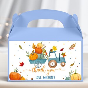 Può includere: Scatola regalo blu con un'etichetta bianca che presenta un'illustrazione di un camioncino blu che trasporta zucche. L'etichetta include anche il testo "grazie" e "Con affetto, Wilson's".
