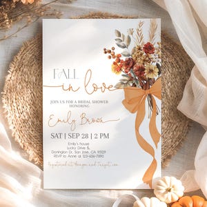 May include: Bridal shower invitation with the text "Fall in Love" and details for Emily Brown's shower. The invitation features a floral bouquet with orange and red flowers and a large orange bow. The background is a neutral color.