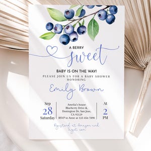 Op de afbeelding: Een uitnodiging voor een babyshower met een aquarel illustratie van bosbessen en groene bladeren. De uitnodigingstekst luidt: "A Berry Sweet, Baby is on the Way!" en bevat details over het evenement.
