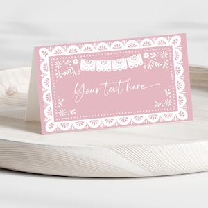 Könnte beinhalten: Eine rosa gefaltete Karte mit weißem Zierrand und dem Text "Your text here". Die Karte hat einen gewellten Rand und florale und Banner-Akzente. Die Karte wird auf einem hellen Holztablett präsentiert.