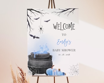 May include: A welcome sign for a baby shower with a Halloween theme. The sign features a black cauldron with blue smoke, a blue pumpkin, and a bottle of potion. The text on the sign reads "Welcome to Emily's Baby Shower 10.28.2058".