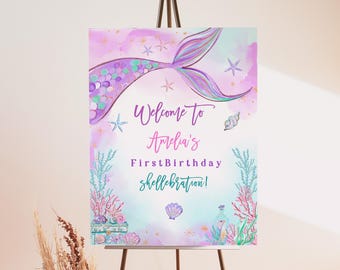 May include: A welcome sign for a first birthday party with a mermaid tail, seashells, and stars on a pink and blue watercolor background. The text reads "Welcome to Amelia's First Birthday Shell-ebration!"