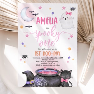May include: A pink and purple Halloween-themed first birthday party invitation with a ghost, a cauldron, a black cat, and stars. The invitation says "Amelia is a spooky one" and includes the date, time, and location of the party.