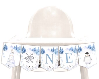 May include: A blue and white high chair banner with a winter theme. The banner features a polar bear, an owl, a snowflake, penguins, and the letters "ONE".