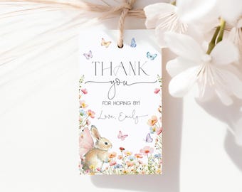 Könnte beinhalten: Ein weißes Geschenk-Etikett mit den Worten "THANK you" und "FOR HOPING BY!" in Schwarz gedruckt. Das Etikett zeigt eine Aquarell-Illustration eines Hasen mit Schmetterlingsflügeln, Blumen und Schmetterlingen. Oben ist eine Schnur aus Bindfaden befestigt.