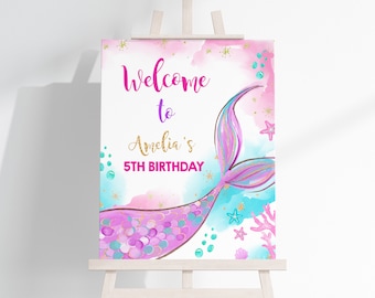 May include: Welcome to Amelia's 5th Birthday sign with a pink and blue mermaid tail with gold glitter accents. The background is a watercolor wash of pink and blue with gold glitter and starfish.