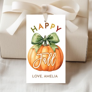 May include: A white gift tag with a watercolor pumpkin design. The tag reads "HAPPY FALL" in green, orange, and red lettering, with a green bow. The tag also includes the text "LOVE, AMELIA".