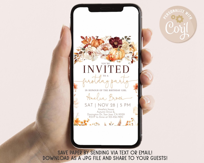 May include: A smartphone displays a digital invitation for a first birthday party. The invitation features a floral arrangement with pumpkins and fall foliage. Text includes the event details and the phrase "You're Invited".