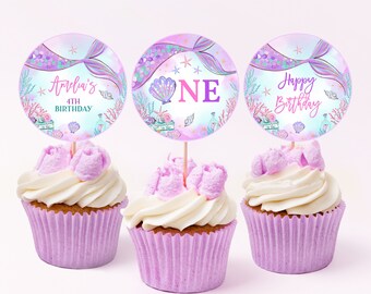 May include: Three purple and blue cupcake toppers with a mermaid tail, seashells, and stars. The toppers say "Amelia's 4th Birthday", "One", and "Happy Birthday".