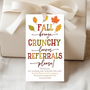 May include: A gift tag with fall-themed graphics and text. The tag features colorful leaves and the words "FALL breeze CRUNCHY leaves REFERRALS please!" in various fonts and colors. The tag is attached to a wrapped gift with a white ribbon.
