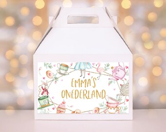 Op de afbeelding: Witte cadeaudoos met een kleurrijk Alice in Wonderland-thema. De doos heeft een handvat en bevat een roze theepot, flamingo, speelkaarten en een cupcake. De tekst op de doos luidt "Emma's Onederland".