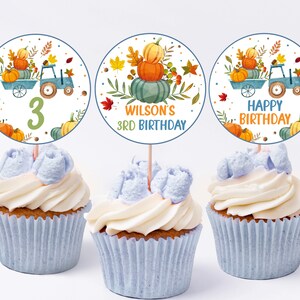 Op de afbeelding: Drie ronde cupcake-toppers met een herfstthema. De toppers tonen een blauwe vrachtwagen met pompoenen, herfstbladeren en de tekst "Wilson's 3rd Birthday" en "Happy Birthday".